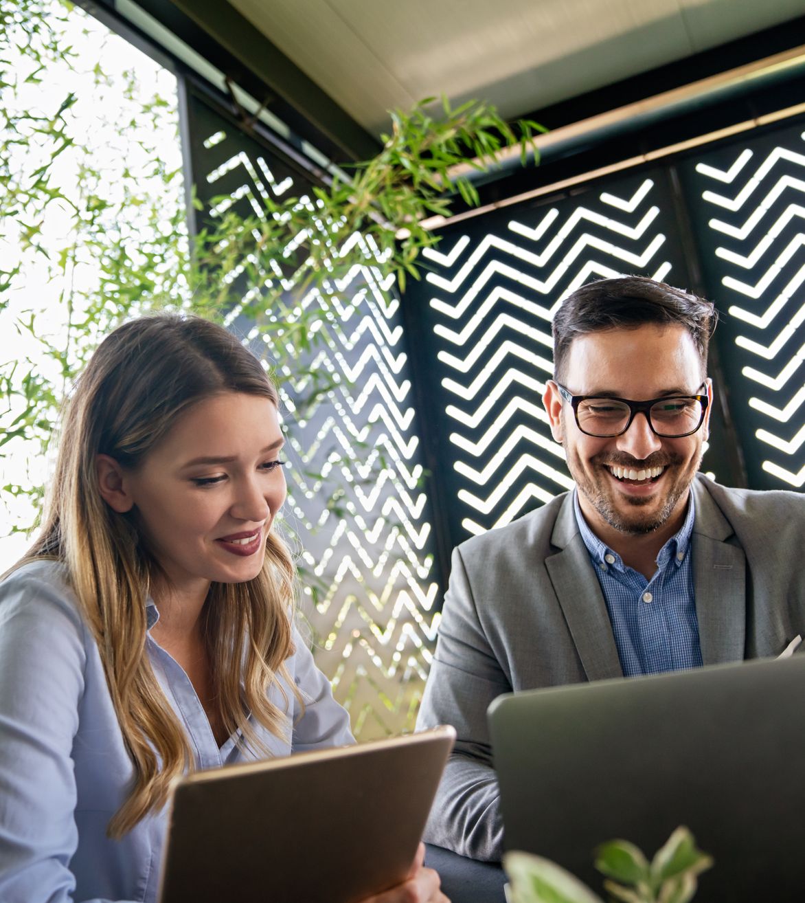 two corporate workers smiling at their laptops