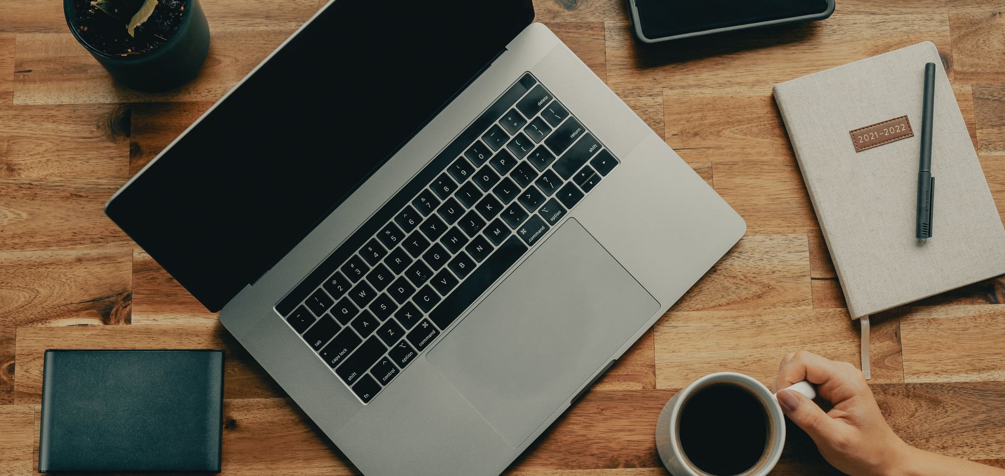 A laptop rests on an oak desk with a cup of coffee next to it