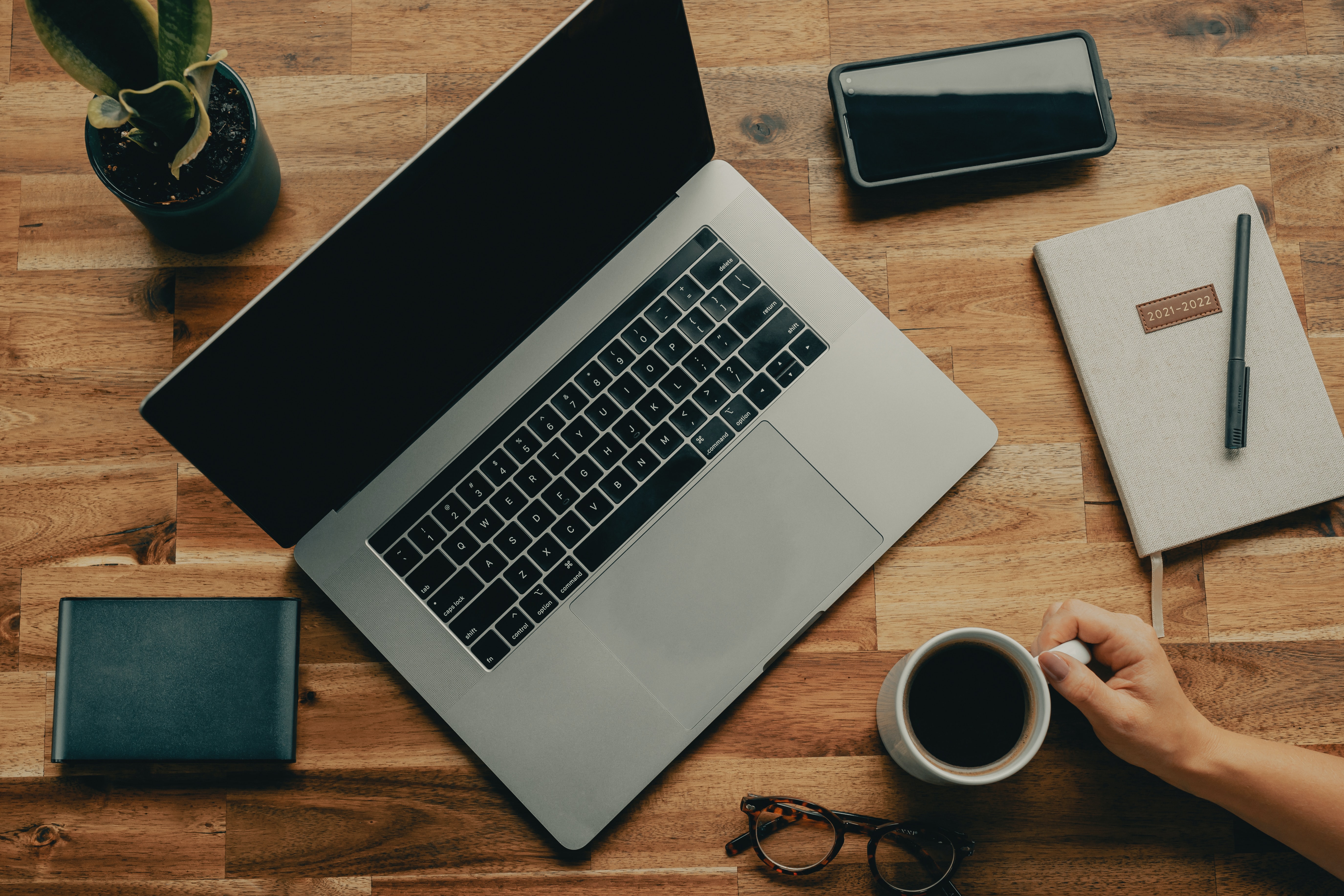 A laptop rests on an oak desk with a cup of coffee next to it