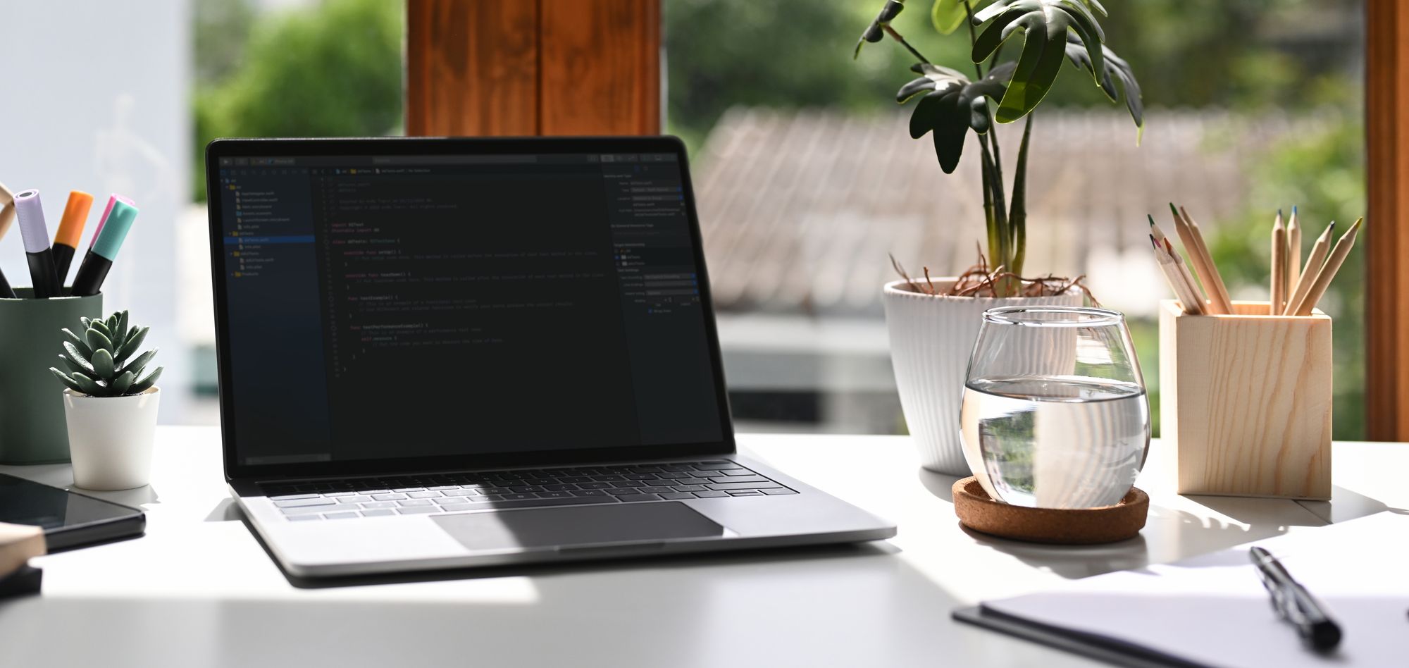 A desk with a laptop, notepad and glass of water