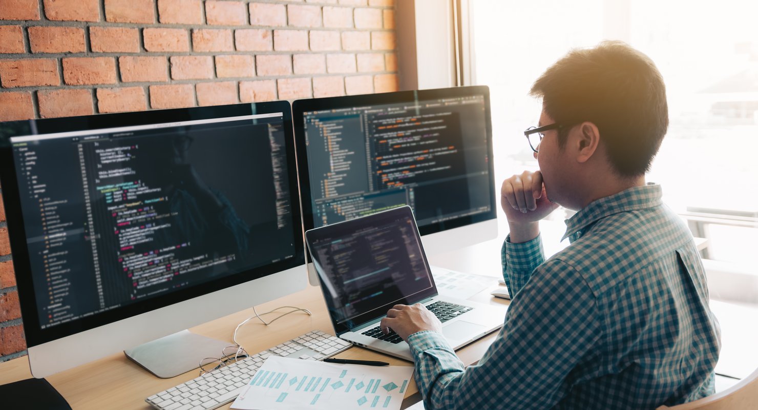 Developer writing a custom-coded website behind 2 screens.