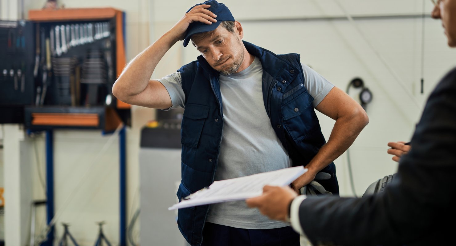 A tradesman in a workshop looks frustrated, struggling to find leads. He needs help with his website to get more jobs.