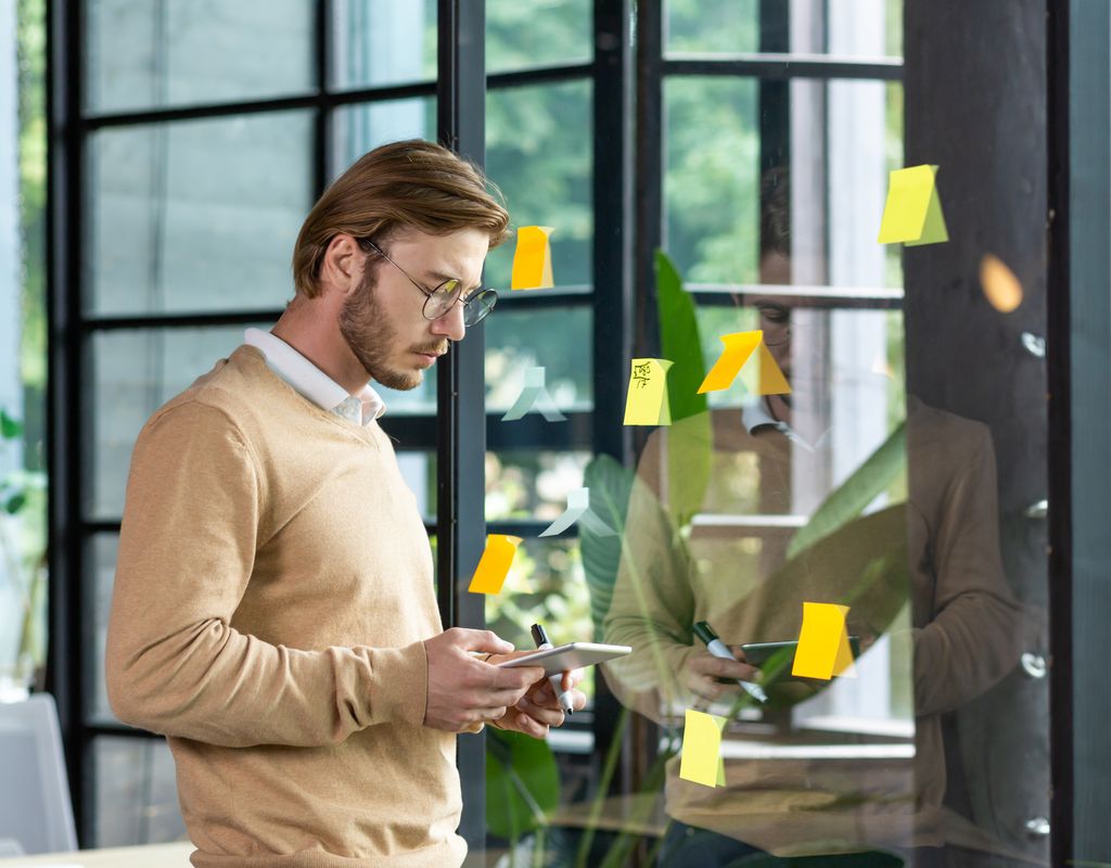 A man, surrounded by sticky notes, looking at a tablet