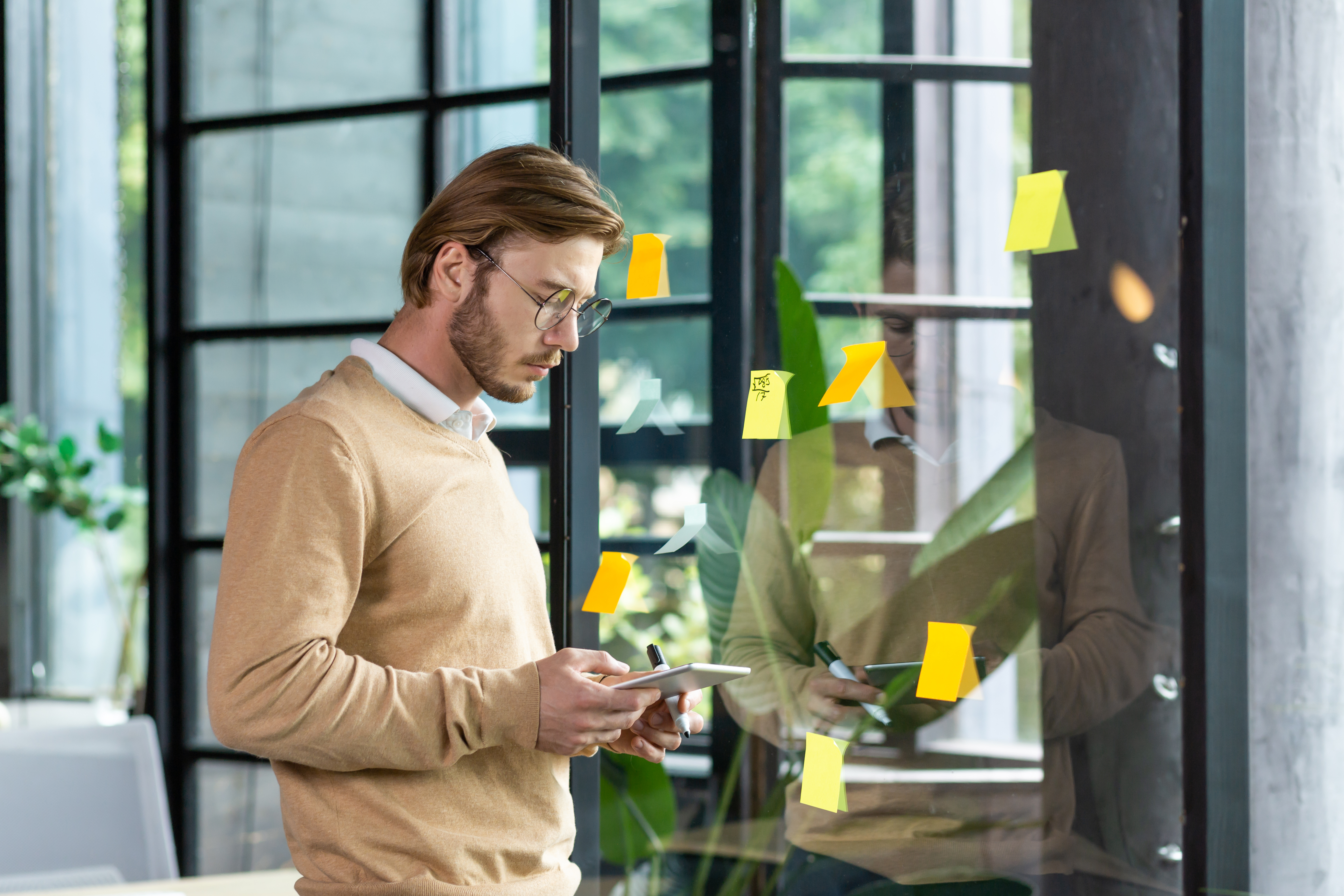 A man, surrounded by sticky notes, looking at a tablet