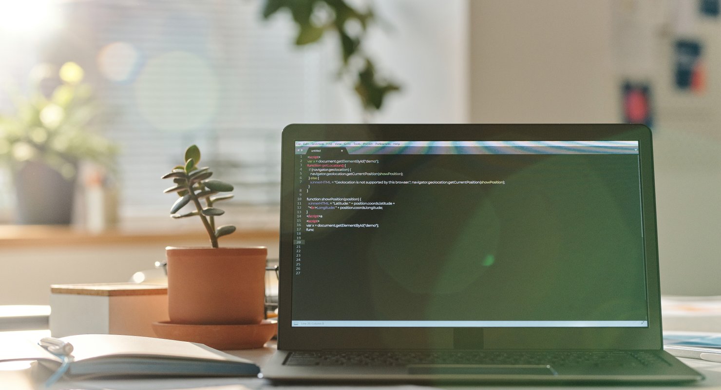 A picture of a laptop that has code on next to a pot plant, ready to create an SEO friendly website.