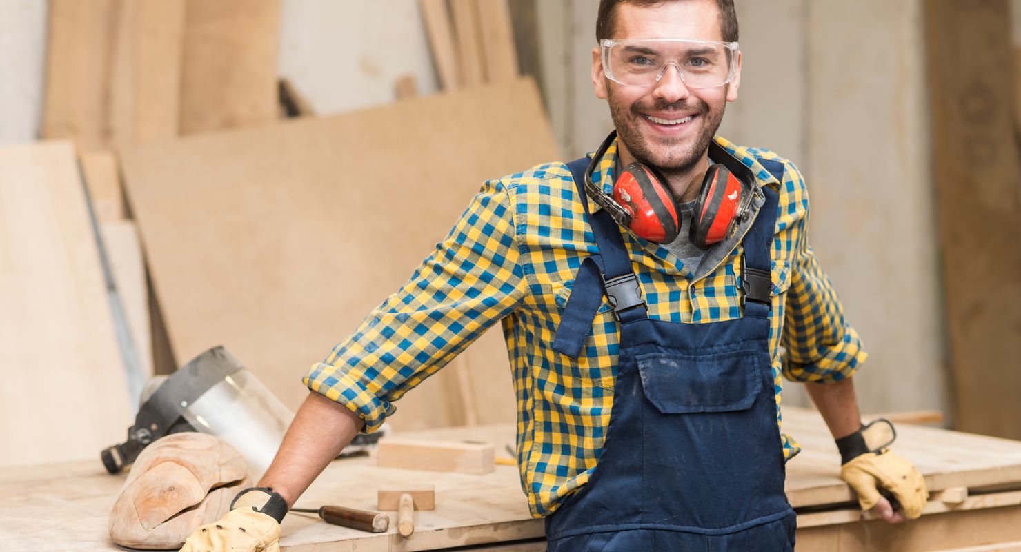 Smiling tradesman looking towards a camera while by a workbench.