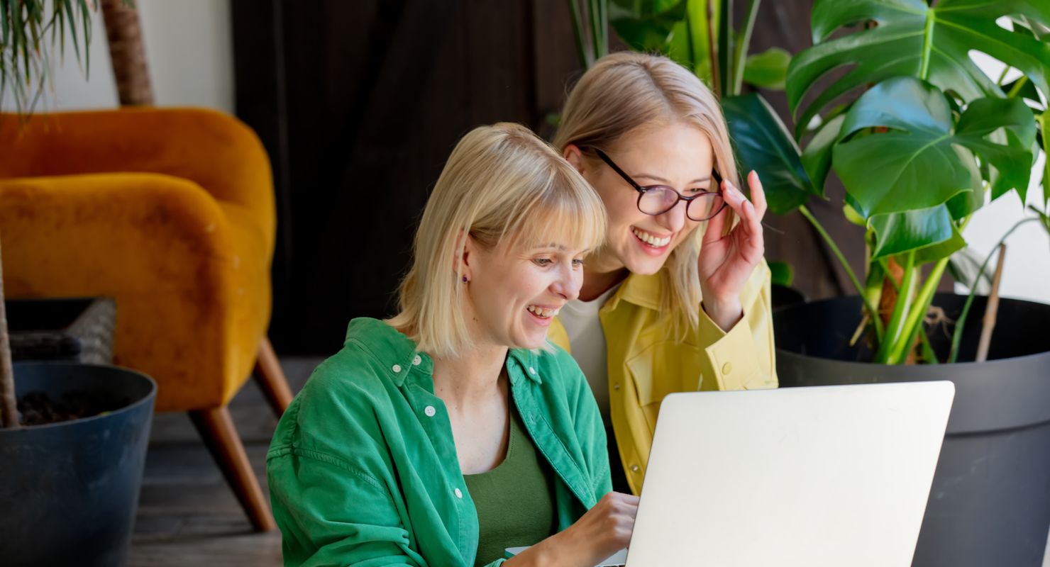 Two women huddled over a laptop, working and smiling