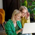 Two women huddled over a laptop, working and smiling