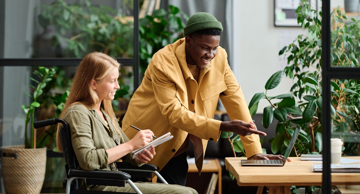 Young man pointing at a computer screen while a woman takes notes.